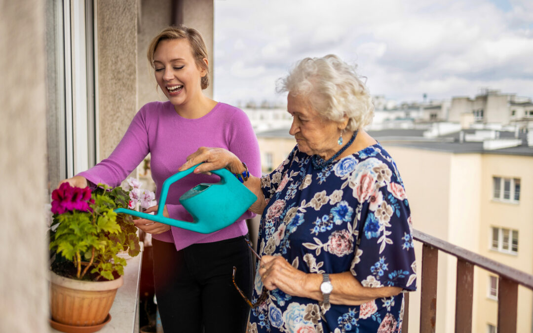 Aide à domicile avec koappy - Une jeune femme aide une personne âgée à arroser ses plantes sur un balcon